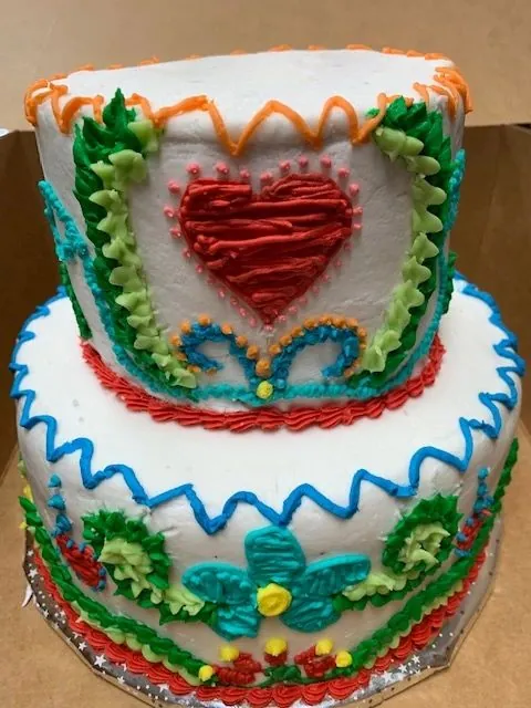 Two-tier white cake with piped red heart and blue and green floral details