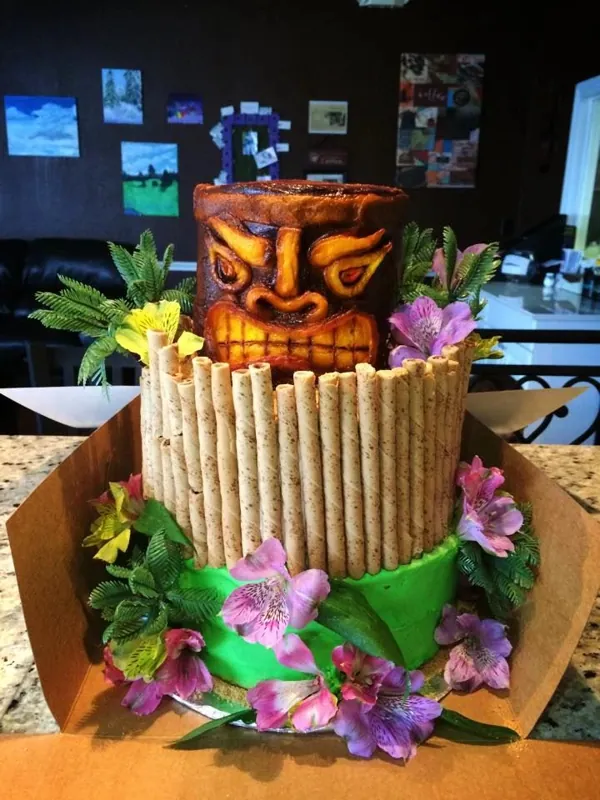 Tiki-themed cake with a carved mask, bamboo fence and tropical flowers
