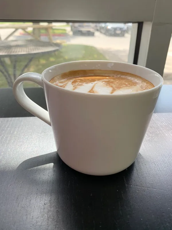 A hot latte in a white mug by the front window